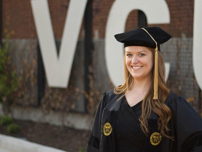 Heather Caslin in graduation regalia standing in front of a VCU sign