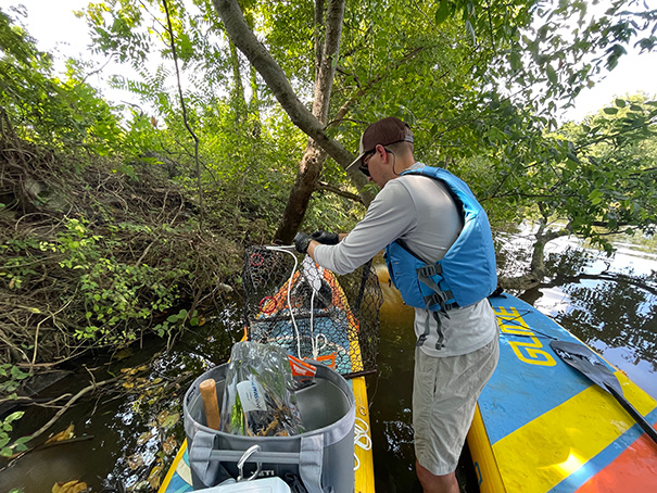 Thomas Dunlap stands between two rafts near the riverbank, holding up netting