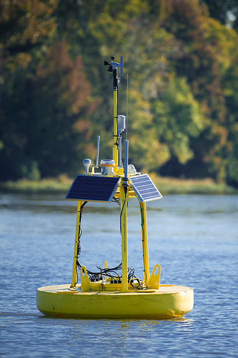 A yellow buoy with solar panels and wire sits on still water