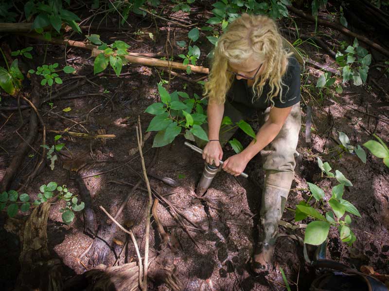 A students sitting on the ground uses hand-drill in the dirt